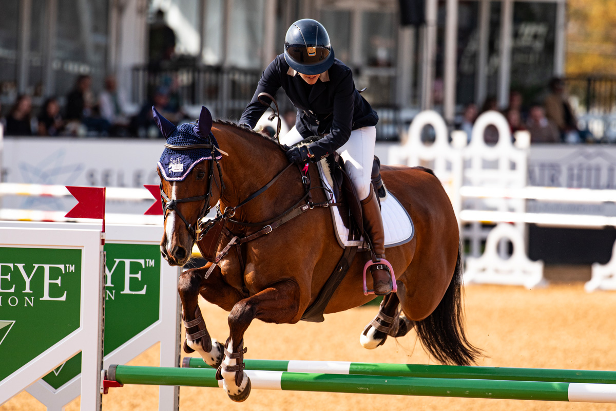 horse and rider suspended in the air over a jump. The horses' legs ar tucked up under it.