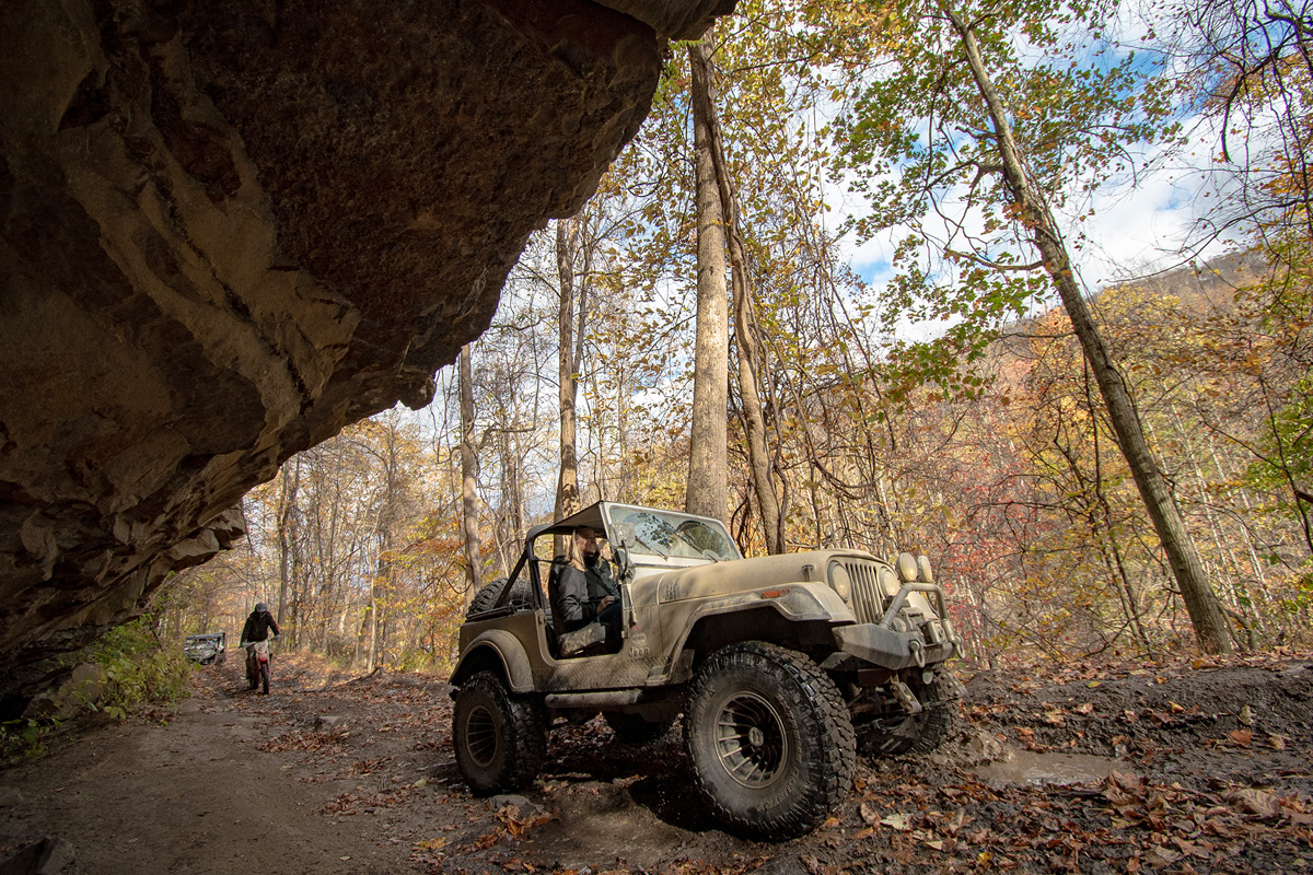 Jeep driving under a giant rock overhang with a mountain in the distance